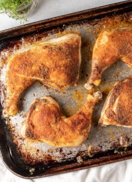 Roasted chicken legs topped with seasonings on a baking sheet