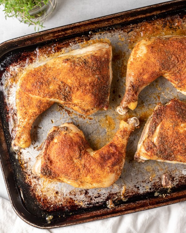 Roasted chicken legs topped with seasonings on a baking sheet