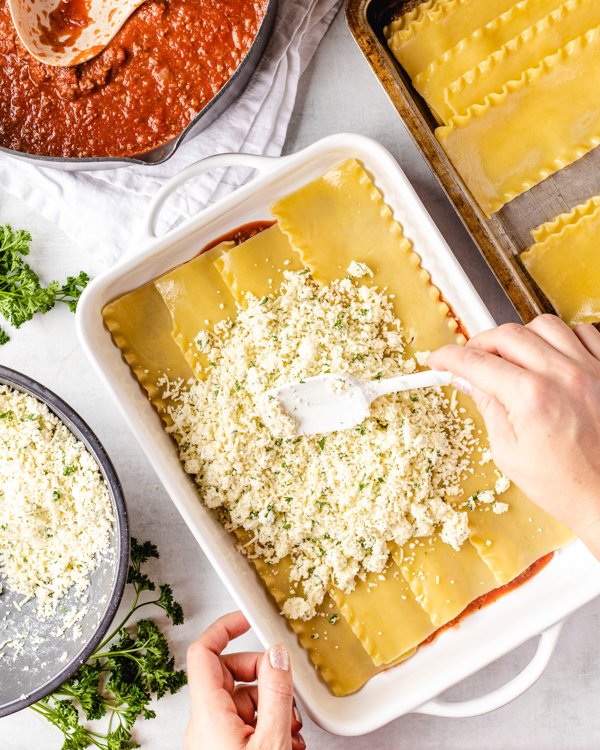 spreading cheese on lasagna noodles in a pan