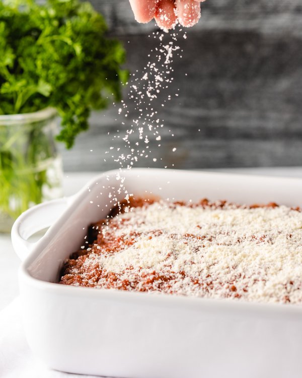 sprinkling parmesan over a pan of unbaked lasagna