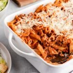 venison pasta bake in a white baking dish with salad and bread in the background