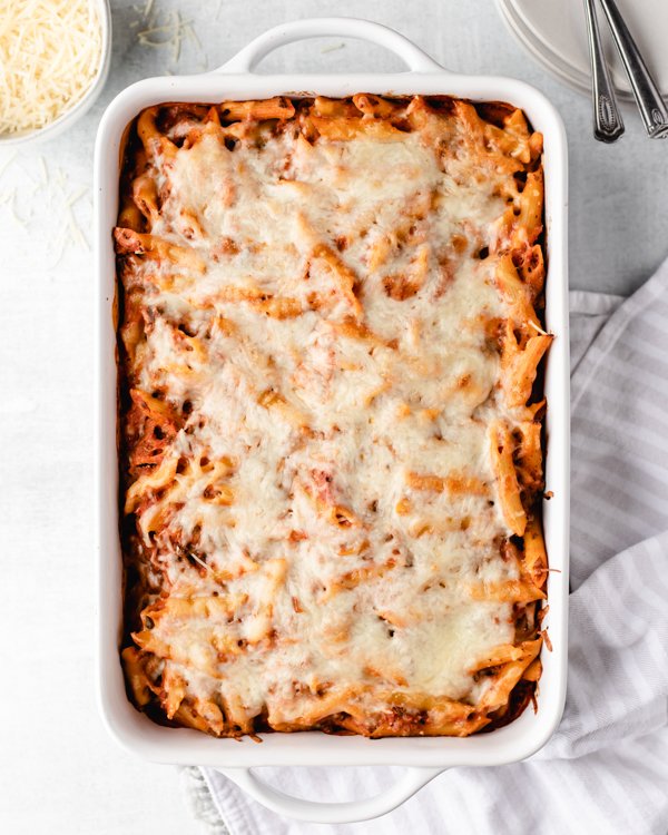 venison pasta bake in a white baking dish with salad and bread in the background