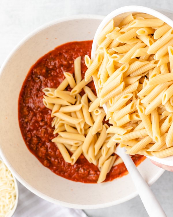 pouring penne pasta into a bowl of red sauce