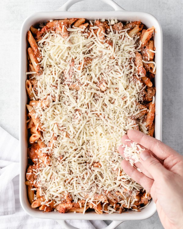 sprinkling cheese on venison pasta bake on a white baking dish