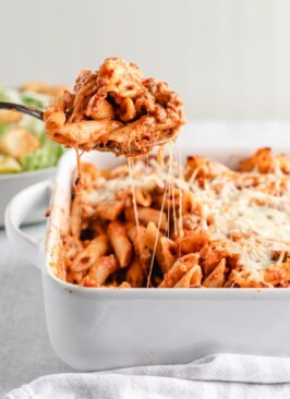 venison pasta bake in a white baking dish with salad and bread in the background