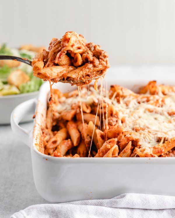 venison pasta bake in a white baking dish with salad and bread in the background