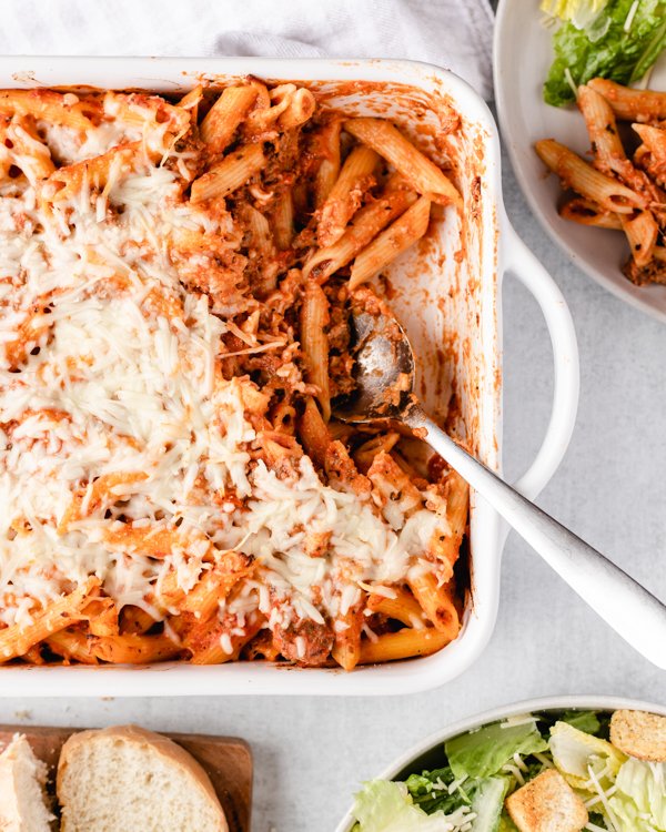 venison pasta bake in a white baking dish with salad and bread in the background