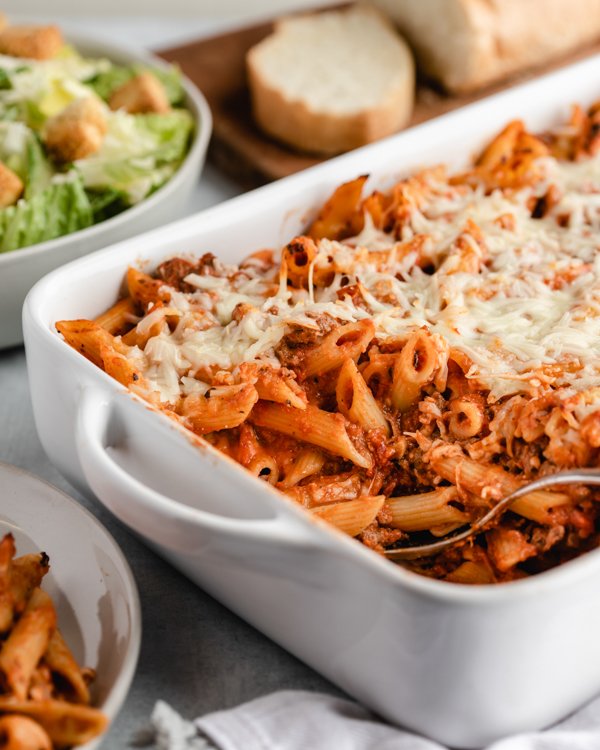 venison pasta bake in a white baking dish with salad and bread in the background