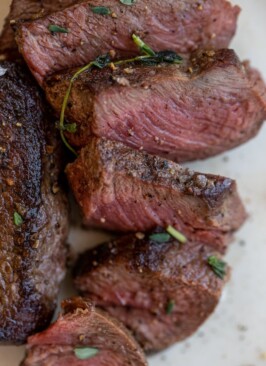 venison chops sliced on a white plate with salt and thyme