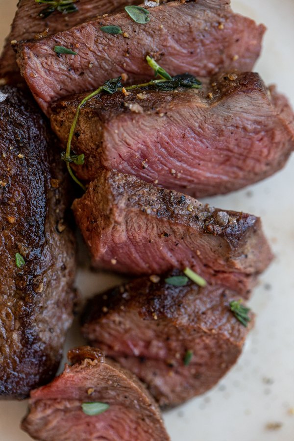 venison chops sliced on a white plate with salt and thyme