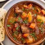 slow cooker venison stew in an orange bowl on a blue plate with a piece of bread