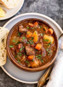 slow cooker venison stew in an orange bowl on a blue plate with a piece of bread
