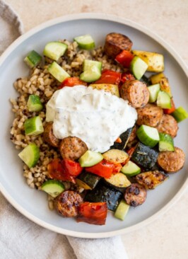 Italian sausage and veggie bowls with tzatziki sauce on blue bowls