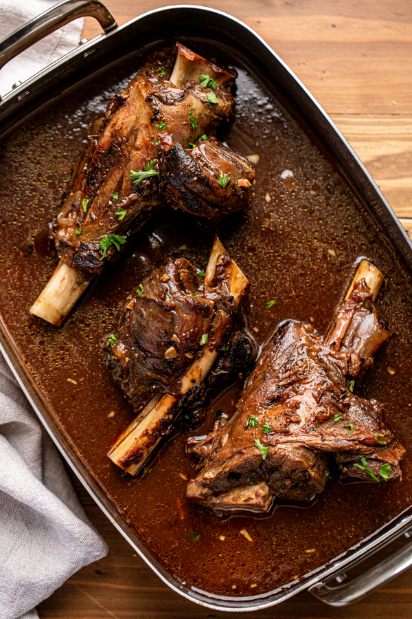 venison shank in a roasting dish with braising liquid 