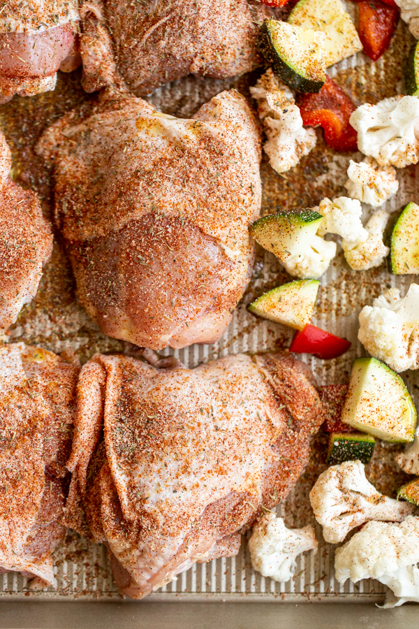uncooked chicken thighs with vegetables on a baking sheet