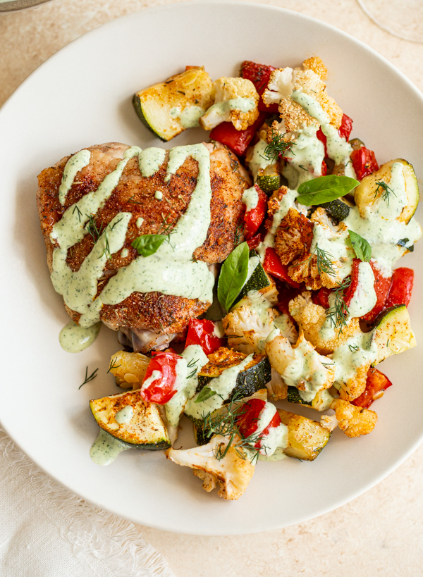 sheet pan chicken thigh dinner with veggies and a green herb sauce on a plate