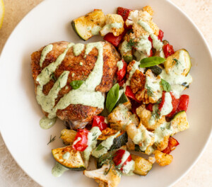 sheet pan chicken thigh dinner with veggies and a green herb sauce on a plate