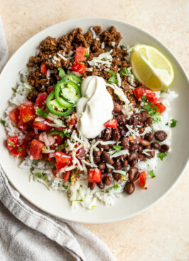 venison burrito bowls with sour cream, cheese and black beans in a white bowl