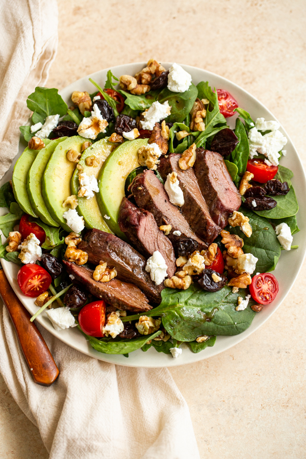 venison steak salad in a bowl with goat cheese, tomatoes, avocado and walnuts