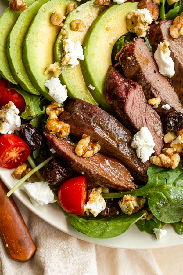 venison steak salad in a bowl with goat cheese, tomatoes, avocado and walnuts