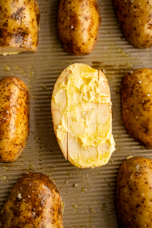 a potato on a baking sheet with cuts in it covered in butter and salt