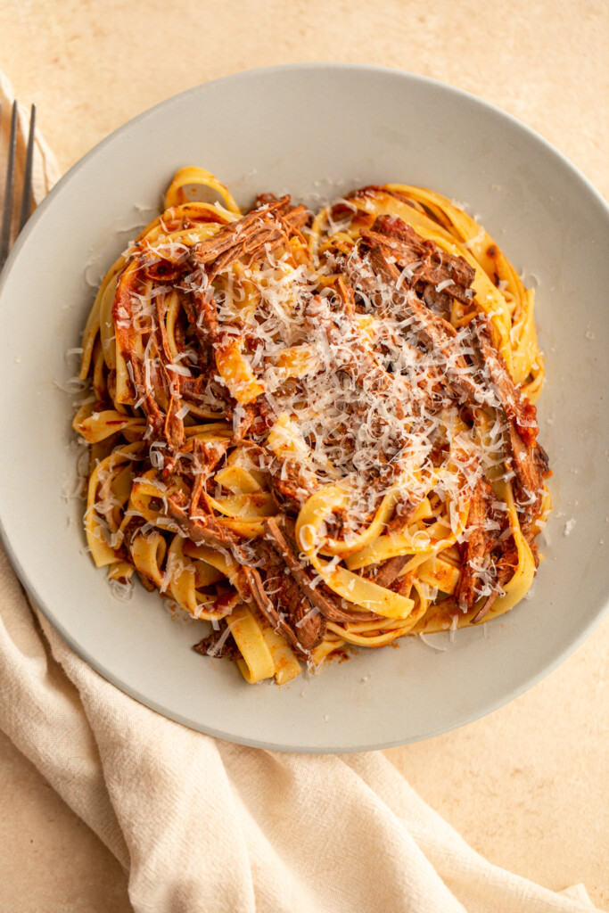 venison ragù on a grey plate with pasta and grated cheese