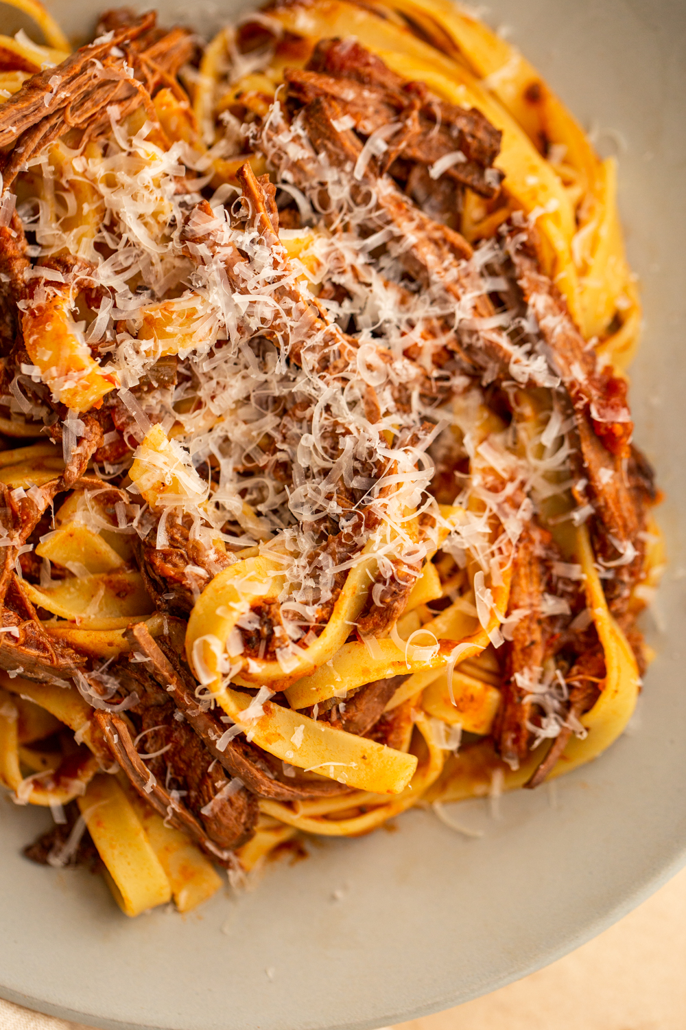 venison ragù on a grey plate with pasta and grated cheese