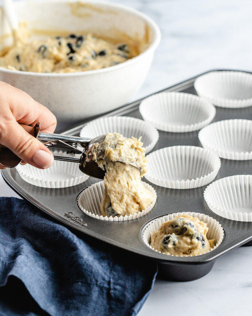 scooping blueberry muffins into a muffin tin