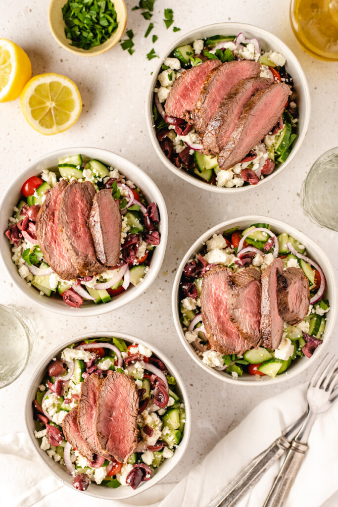 Four prepared Mediterranean Venison Steak Bowl in white bowls with forks and linen