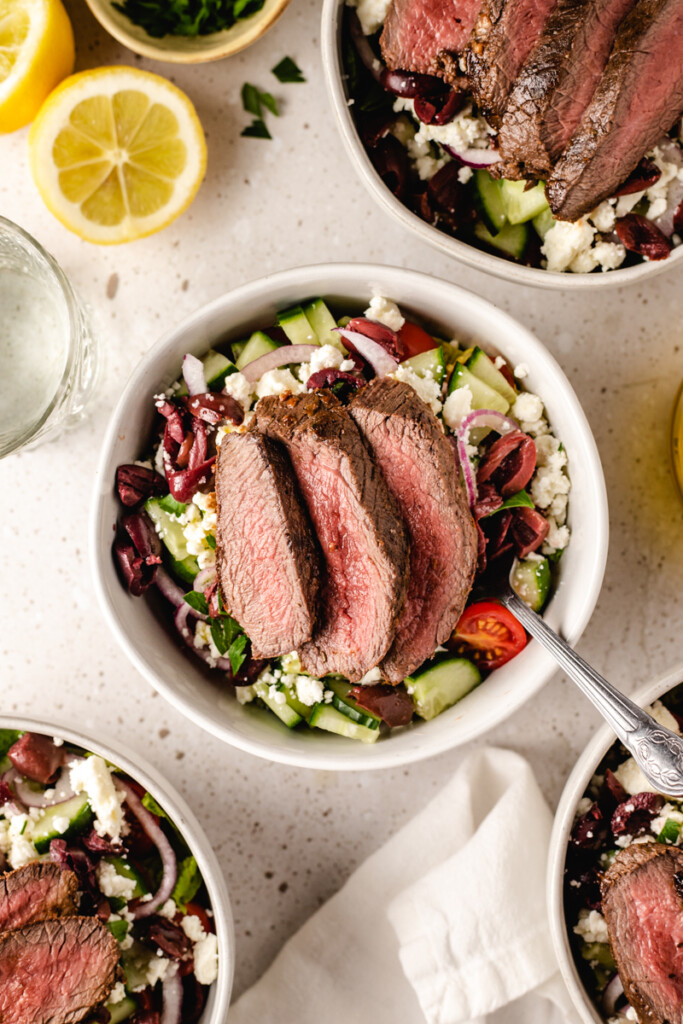 Prepared Mediterranean Venison Steak Bowl in white bowl with fork surrounded by other prepared bowls