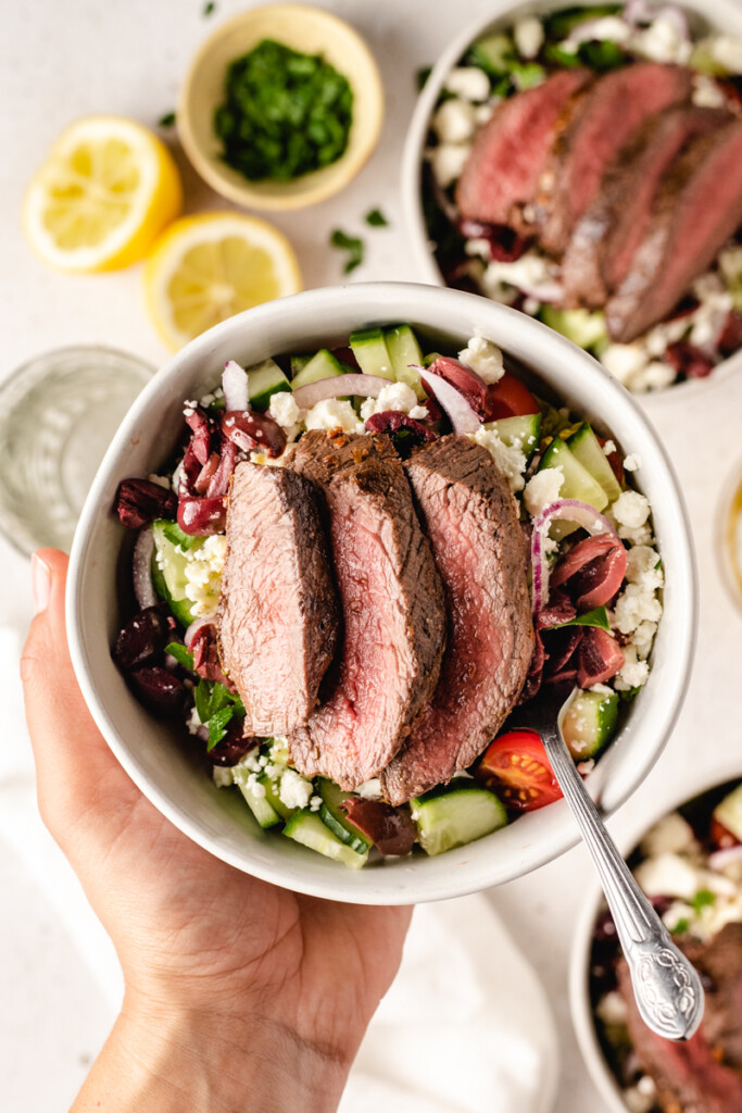 Hand holding a prepared Mediterranean Venison Steak Bowl with a fork in it