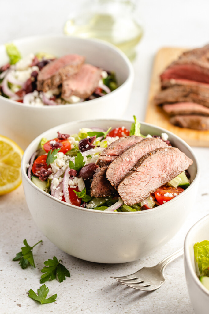 Mediterranean Venison Steak Bowls in white bowl with fork and sliced steak in background