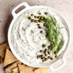 Cottage Cheese Caper Dill Dip in white round dish garnished with fresh dill and capers with crackers beside it