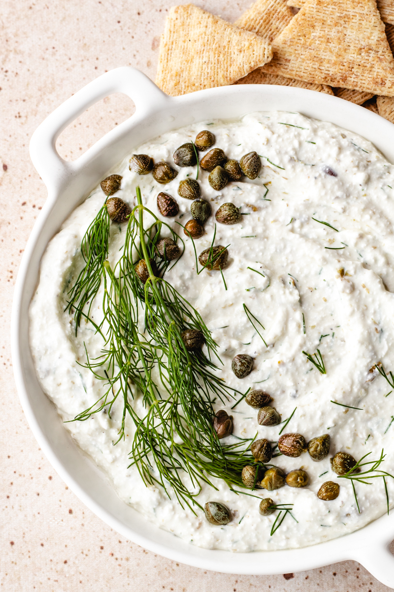 Cottage Cheese Caper Dill Dip in white round dish with crackers beside it