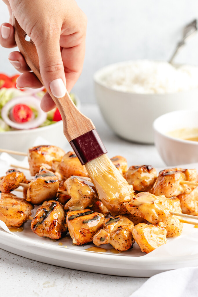 Grilled chicken kebabs being brushed with sauce