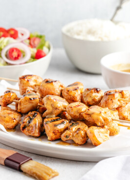 Grilled honey mustard chicken kebabs on white platter surrounded by honey mustard sauce, white rice and salad
