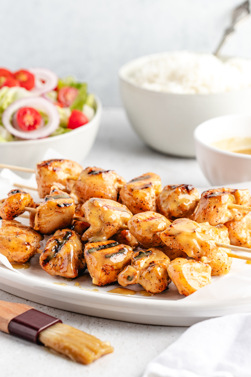 Grilled honey mustard chicken kebabs on white platter surrounded by honey mustard sauce, white rice and salad