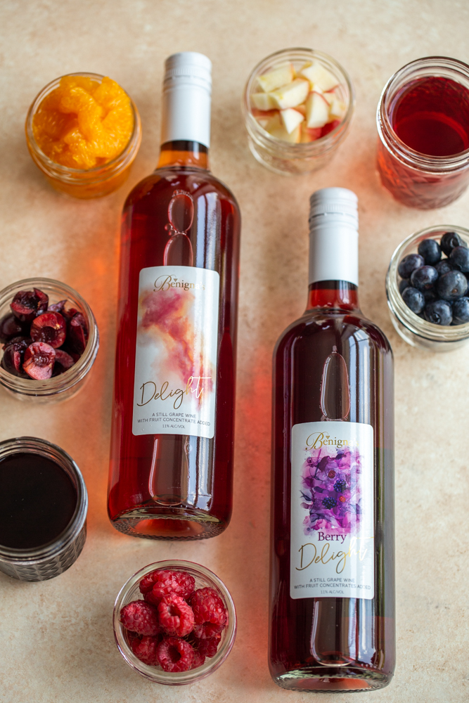 wine with berries, oranges and apples on a cream counter top