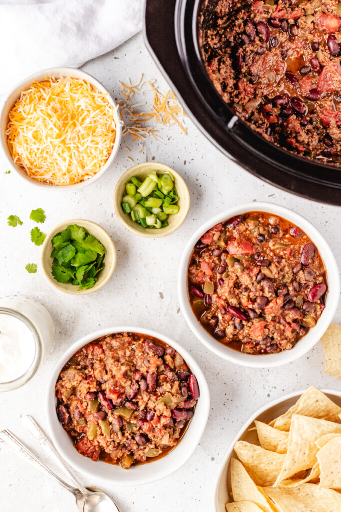 Two bowls of Slow Cooker Venison Chili with toppings around it