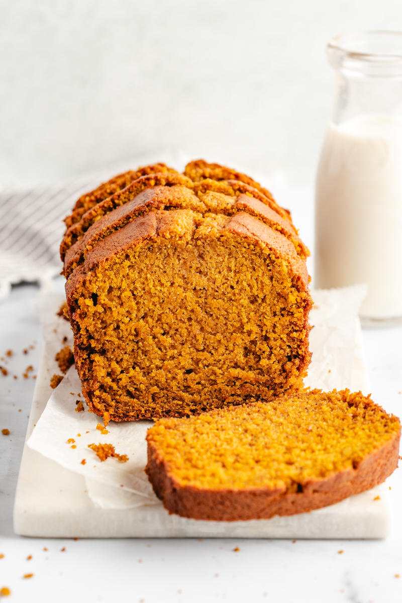 Sliced pumpkin bread on white cutting board with milk in background