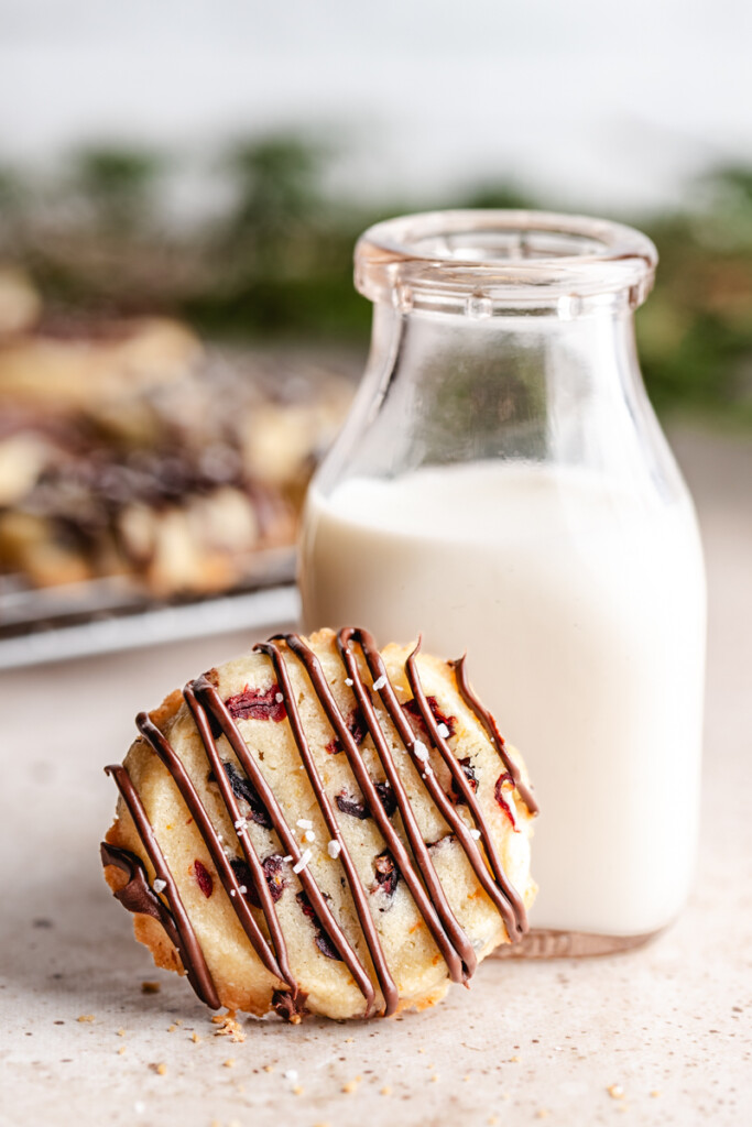 A baked Shortbread Cookie with Orange & Cranberry propped next to small milk jug