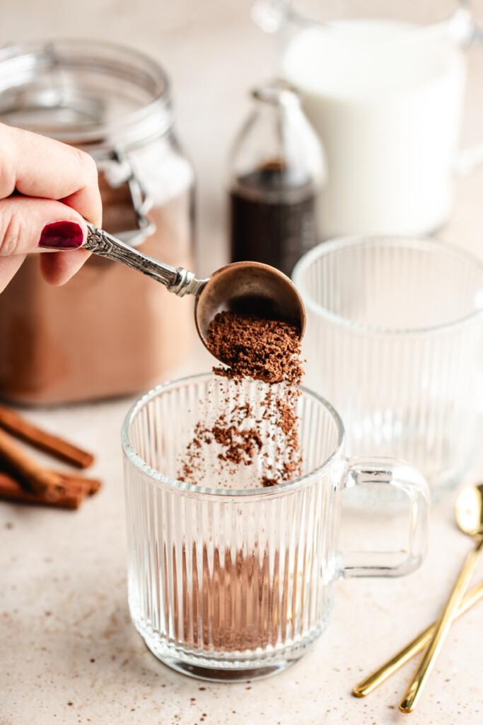 healthier hot cocoa mix being sprinkled into empty glass mug