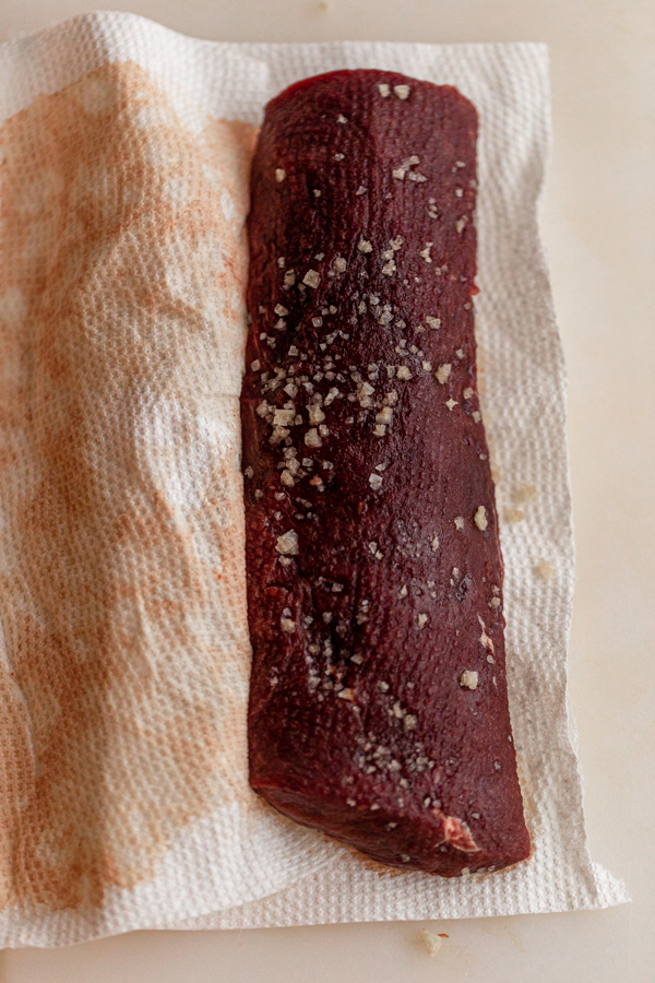 a deer backstrap covered in a salt on a paper towel before cooking