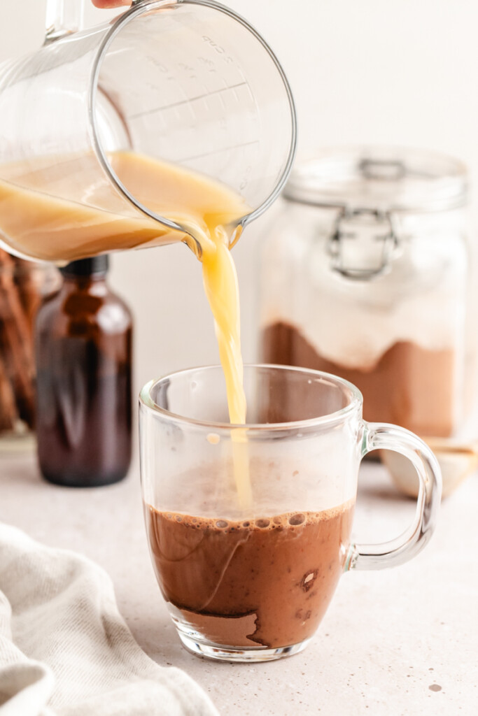 Bone broth being poured over hot chocolate mix in a glass mug