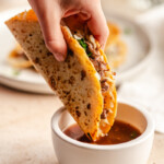 A venison birria taco being dipped in broth