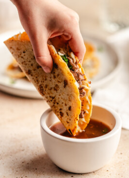 A venison birria taco being dipped in broth