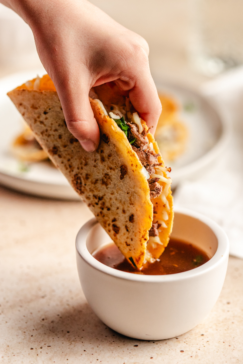 A venison birria taco being dipped in broth