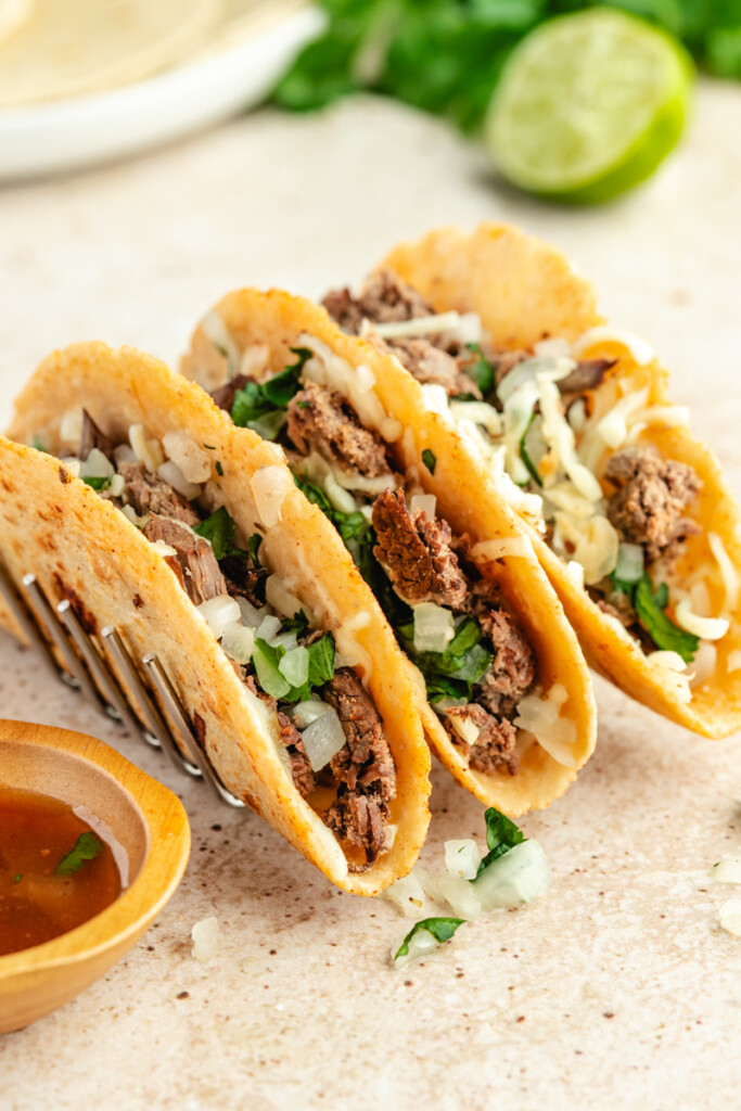 three tacos in a taco holder with broth in small wooden bowl beside it