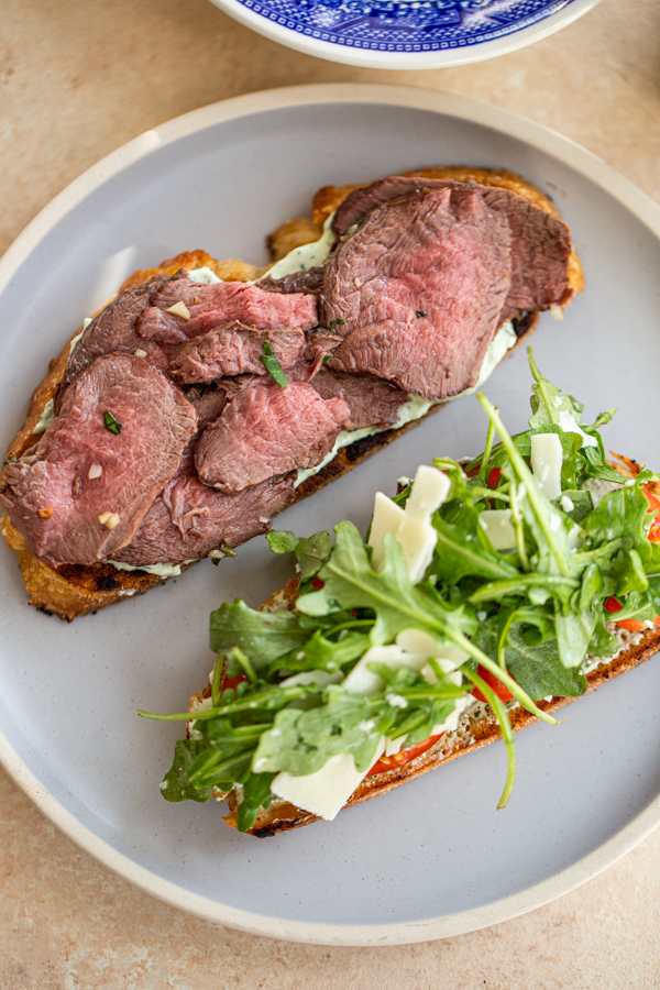 thin sliced venison on a piece of bread with another piece of bread covered with arugula for a venison steak sandwich