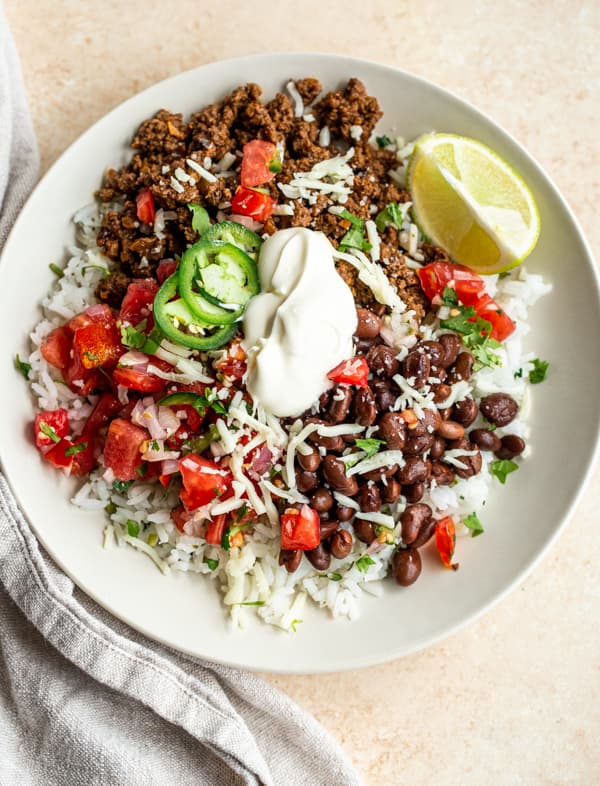 Ground Venison Recipes: venison burrito bowls with sour cream, cheese and black beans in a white bowl